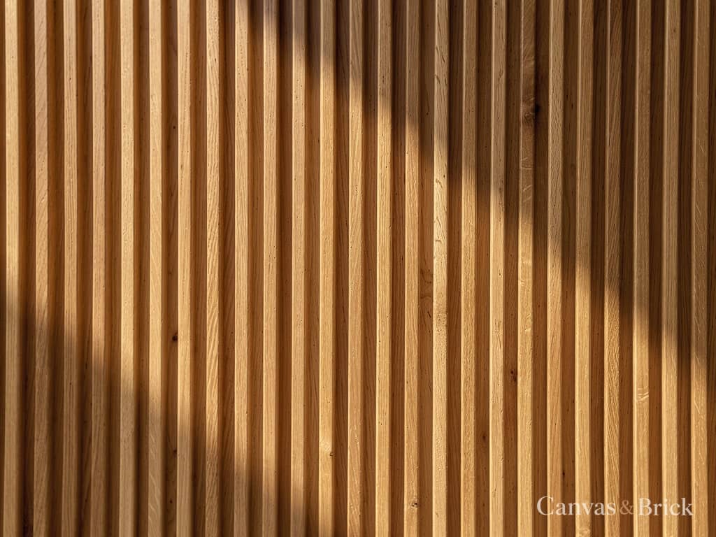 Fluted oak wall panel, vertical half-round battens casting rhythmic parallel shadows