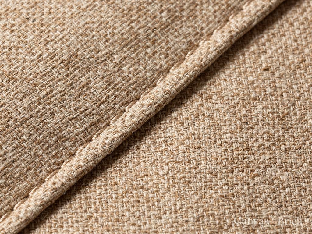 Textured woven upholstery in warm oatmeal, showing the yarns and a piped seam